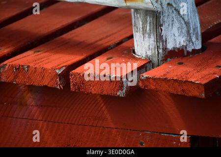 Un dettagliato primo piano di tavole in legno intemperie dipinte in un rosso intenso e vibrante. L'immagine evidenzia la consistenza rustica della vernice di peeling e della st Foto Stock