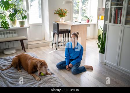 Una donna matura e rilassata, proprietaria di un animale domestico, che riposa e gioca a casa durante il fine settimana con il suo amato cane. Foto Stock