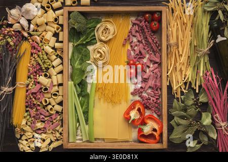 Collage di vari tipi di pasta e verdure disposti in un vassoio di legno con dettagli colorati Foto Stock