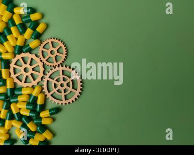 Capsule di gelatina gialla e verde e piccoli ingranaggi di legno su sfondo verde. Foto Stock