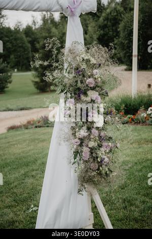 Elegante arco nuziale all'aperto decorato con fiori pastello a cascata, respiro del bambino e vegetazione. Romantica cerimonia sullo sfondo in un giardino naturale Foto Stock