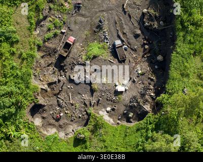 Vista aerea dei camion sparsi in un cantiere edile, in mezzo al forte contrasto tra terra scura e vibrante vegetazione verde, Klaten Regency, Cent Foto Stock