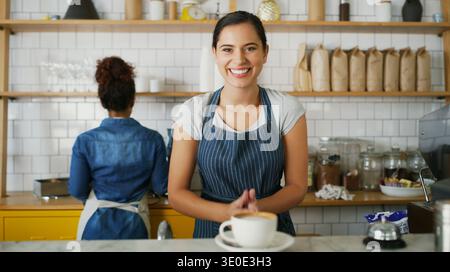 Ritrattista, donna e imprenditrice con un sorriso in caffetteria, ristorante e servizio clienti. Fiducia, manager di caffè e imprenditore Foto Stock