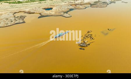 Vista aerea di una barca che affetta attraverso il fiume fangoso, giustapposta alle rive sabbiose, Puerto Maldonado, madre de Dios, Perù. Foto Stock