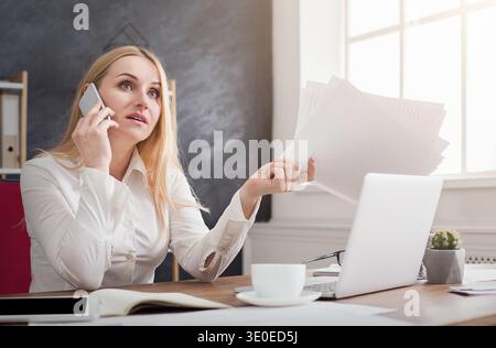 Donna d'affari seria che tiene documenti e parla al telefono Foto Stock