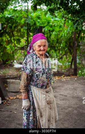 Donna anziana sorridente in un giardino che indossa un velo e un grembiule Foto Stock