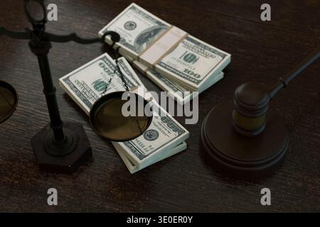 Potente scatto concettuale con pile di banconote da cento dollari bilanciate su bilance legali accanto a un martelletto di legno dei giudici. Rappresenta i costi legali, c Foto Stock