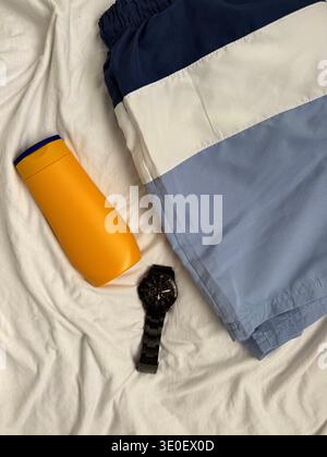 Vista ad angolo alto degli accessori da viaggio estivi da uomo. Flacone in plastica giallo brillante per crema solare o shampoo, eleganti costumi blu navy e blu Foto Stock