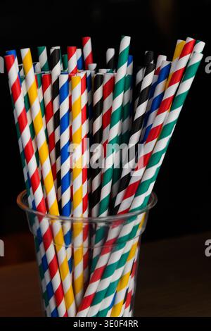 Una tazza di vetro trasparente che contiene cannucce colorate per bere carta con un design colorato a spirale. Foto Stock