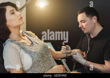 Tatuatore che lavora con ago sul braccio dei clienti Foto Stock