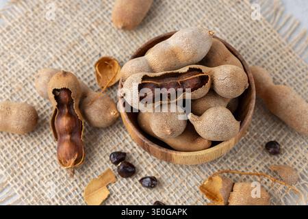 Frutti tamarindi maturi interi e sgusciati con semi in una ciotola di legno in primo piano sullo sfondo della iuta. Cibo esotico sano. Foto Stock