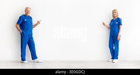 Medici anziani di sesso maschile e femminile che puntano verso uno spazio vuoto tra loro Foto Stock