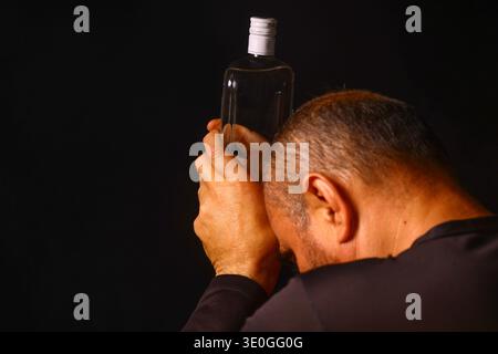 Uomo anziano che tiene una bottiglia in un momento di stanchezza emotiva, che riflette il peso della solitudine, della dipendenza e della tranquilla lotta dell'invecchiamento in è Foto Stock