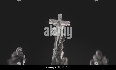 Scultura bianca dettagliata che mostra Gesù Cristo sulla Croce affiancato da figure luttuose contro le tenebre. Simbolo di fede e sacrificio. Concetto religioso di Crocifissione al Calvario. Scena calvario solenne. Foto Stock