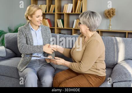 Cliente senior che stringe la mano a una consulente donna nell'accordo di consulenza a domicilio Foto Stock