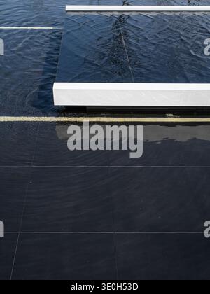 Vista dall'alto verso il basso di una fontana minimalista con piastrelle in pietra nera e finiture bianche. L'immagine trasmette il design dell'acqua, il minimalismo e la geometria. Alta qualità Foto Stock