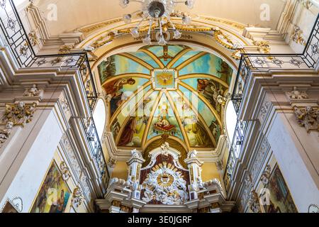 Veduta prospettica della navata nella chiesa della Madonna del Carmine, Ispica. L'interno barocco presenta stucchi bianchi e decorazioni dorate. Pali di legno le Foto Stock