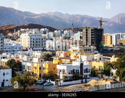 Vista panoramica del quartiere al Khuwair a Mascate, Oman, che mostra un mix di edifici residenziali e nuovi progetti di costruzione sullo sfondo delle aspre montagne Hajar. Foto Stock