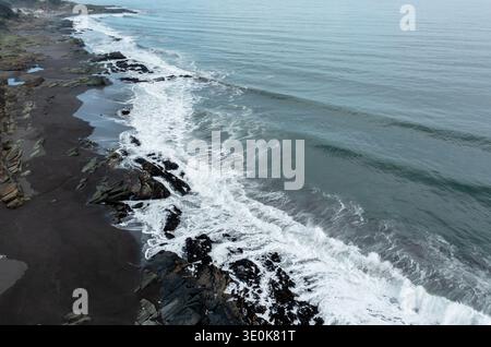 Vista aerea panoramica delle onde che si infrangono sulla costa rocciosa lungo l'oceano durante una giornata nuvolosa Foto Stock