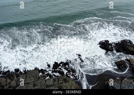 Vista aerea panoramica delle onde che si infrangono sulla costa rocciosa lungo l'oceano durante una giornata nuvolosa Foto Stock