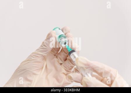 Mani del medico che tengono in mano il flaconcino di vaccino e la siringa durante la preparazione della vaccinazione medica in ambiente sanitario Foto Stock