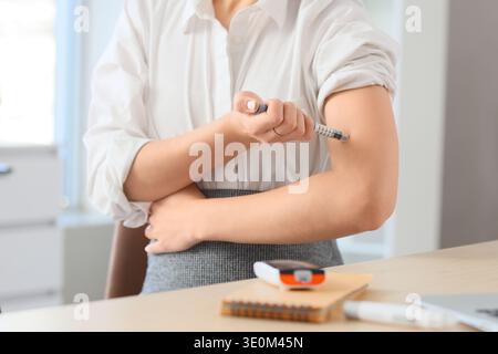 Giovane donna d'affari incinta con diabete gestazionale che usa la lancetta a tavola in ufficio, primo piano Foto Stock