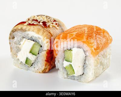 Primo piano di due freschi panini di sushi uramaki giapponesi. Una con salmone d'arancia, l'altra con l'anguilla. Ripieno di formaggio spalmabile e cetriolo. Cibo minimalista Foto Stock