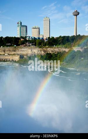 Un vivace arcobaleno attraversa la nebbia delle Cascate del Niagara, Ontario, Canada, con la Skylon Tower e lo skyline della città sullo sfondo. Foto Stock