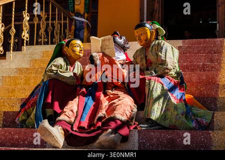 Gli artisti in maschere tradizionali e abiti floreali studiano un testo religioso sui gradini durante il festival Diskit Gustor. Foto Stock