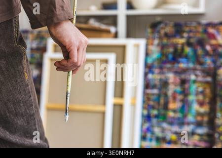 Primo piano della mano di un pittore che tiene un pennello nel suo studio Foto Stock
