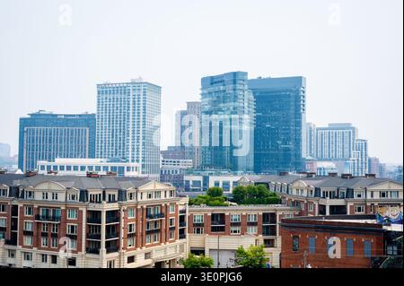 Un paesaggio urbano di Baltimora, Maryland, caratterizzato da un mix di alti edifici moderni e vecchie strutture residenziali con tetto in mattoni sotto un cielo nuvoloso. Foto Stock