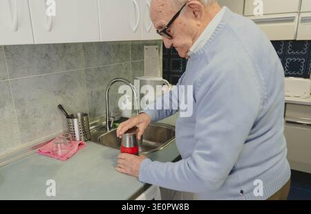 Uomo anziano che prepara una moka nella sua cucina di casa Foto Stock
