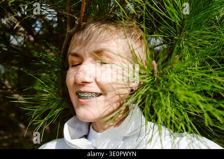 Ritratto di una donna felice sorridente con l'apparecchio ortodontico mentre si gode la natura. Giovane donna adulta con apparecchi dentali all'aperto tra alberi e fiori Foto Stock
