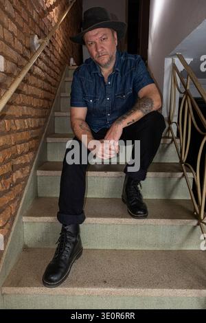 Un brasiliano di 48 anni con tatuaggi siede su una scala e fissa la camera Vertical. Foto Stock