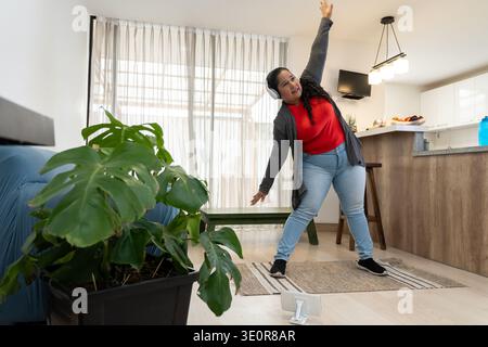 Donna con cuffie che si allunga, fa esercizi di fitness in salotto utilizzando un dispositivo intelligente per la guida Foto Stock