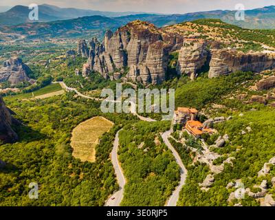 Vista aerea delle spettacolari formazioni rocciose che sorgono in mezzo a una vegetazione lussureggiante, una strada tortuosa che conduce ai monasteri arroccati sulla cima delle scogliere, Météores, Trikala, G. Foto Stock