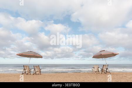 Due ombrelloni da spiaggia a righe con sedie a sdraio vuote di fronte all'oceano sotto il cielo nuvoloso, San Pancho, Nayarit, Messico Foto Stock