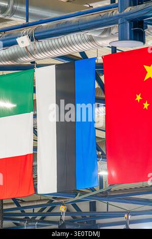 Fila di bandiere nazionali appese a un fascio a soffitto, in uno spazio interno con illuminazione artificiale uniforme le bandiere includono blu con frange bianche e strie rosse Foto Stock