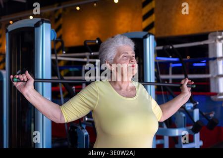 Donna anziana attiva che esegue esercizi di stretching con fitness stick in palestra. Concetto di invecchiamento sano, mobilità, flessibilità e stile di vita attivo per Foto Stock