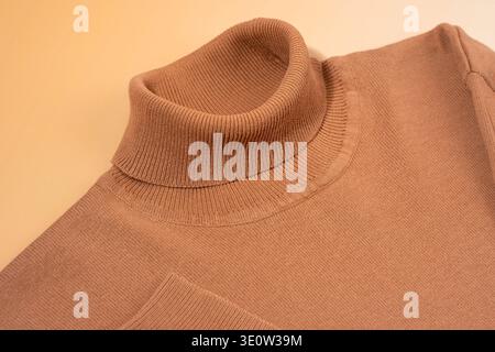 Comodo pullover dolcevita a coste, piatto, lavorato a maglia beige e tonalità cammello su sfondo color pesca pastello. Concetto di base neutrale per il genere, primavera autom Foto Stock