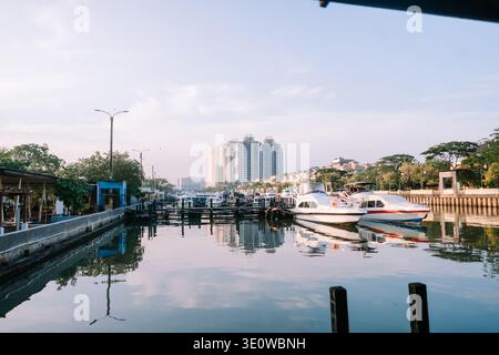 Una tranquilla vista sul canale urbano con barche attraccate lungo il lungomare, con riflessi di moderni edifici alti e residenziali Foto Stock