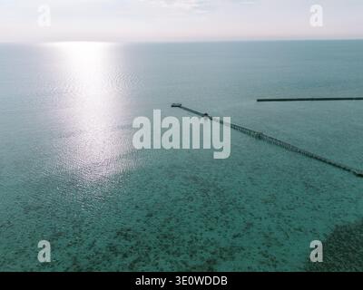 Uno scatto aereo cattura un bellissimo lungo molo in legno che si estende attraverso l'oceano turchese cristallino. L'acqua poco profonda rivela una vivace forma corallina Foto Stock
