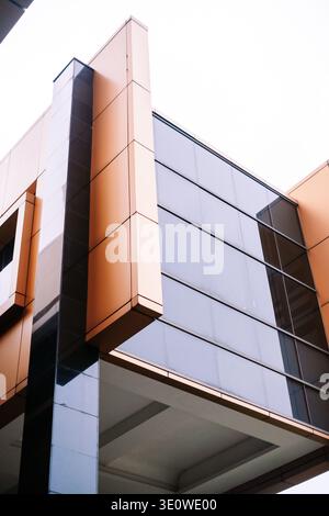 Vista ad angolo basso della facciata di un edificio moderno che presenta pannelli di vetro riflettenti e suggestivo rivestimento in bronzo dorato. Linee geometriche e design contemporaneo Foto Stock