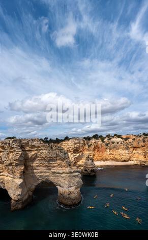 Una vista mozzafiato ad alto angolo delle iconiche scogliere calcaree dorate e degli archi marini naturali lungo la costa dell'Algarve. Si vedono diversi kayak colorati Foto Stock