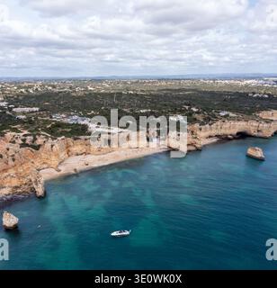 Questa ampia fotografia aerea cattura le iconiche scogliere calcaree dorate e le acque cristalline turchesi della costa dell'Algarve. Un whi solitario Foto Stock