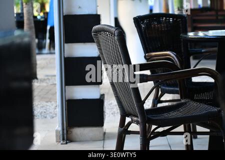 Eleganti sedie in vimini nero disposte su una tranquilla terrazza all'aperto, che sfoggiano intricate trame intrecciate e un'atmosfera sofisticata in stile bistrot Foto Stock