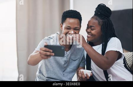 Coppia felice, selfie e maschera per la cura della pelle a casa con legame, giocosa e ridere in camera da letto. Donna nera, uomo e crema con dermatologia, lozione o. Foto Stock