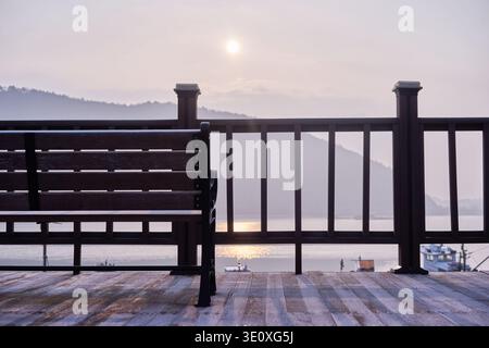Tramonto malinconico al porto di Mangdeok, caratterizzato da un tranquillo ponte in legno, una panchina vuota e un caffe' vintage rosa sbiadito, che evoca nostalgia e solitudine. Foto Stock