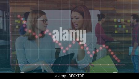 Due donne che parlano con un notebook, indossano una blusa blu, un maglione bianco in ufficio con un grafico per appunti Foto Stock