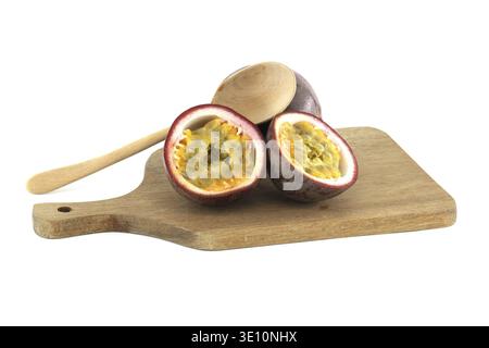 Due frutti della passione tagliati a metà mostrano la loro polpa e i loro semi, stesi su un tagliere di legno con un frutto della passione intero e un cucchiaio di legno che riposa Foto Stock